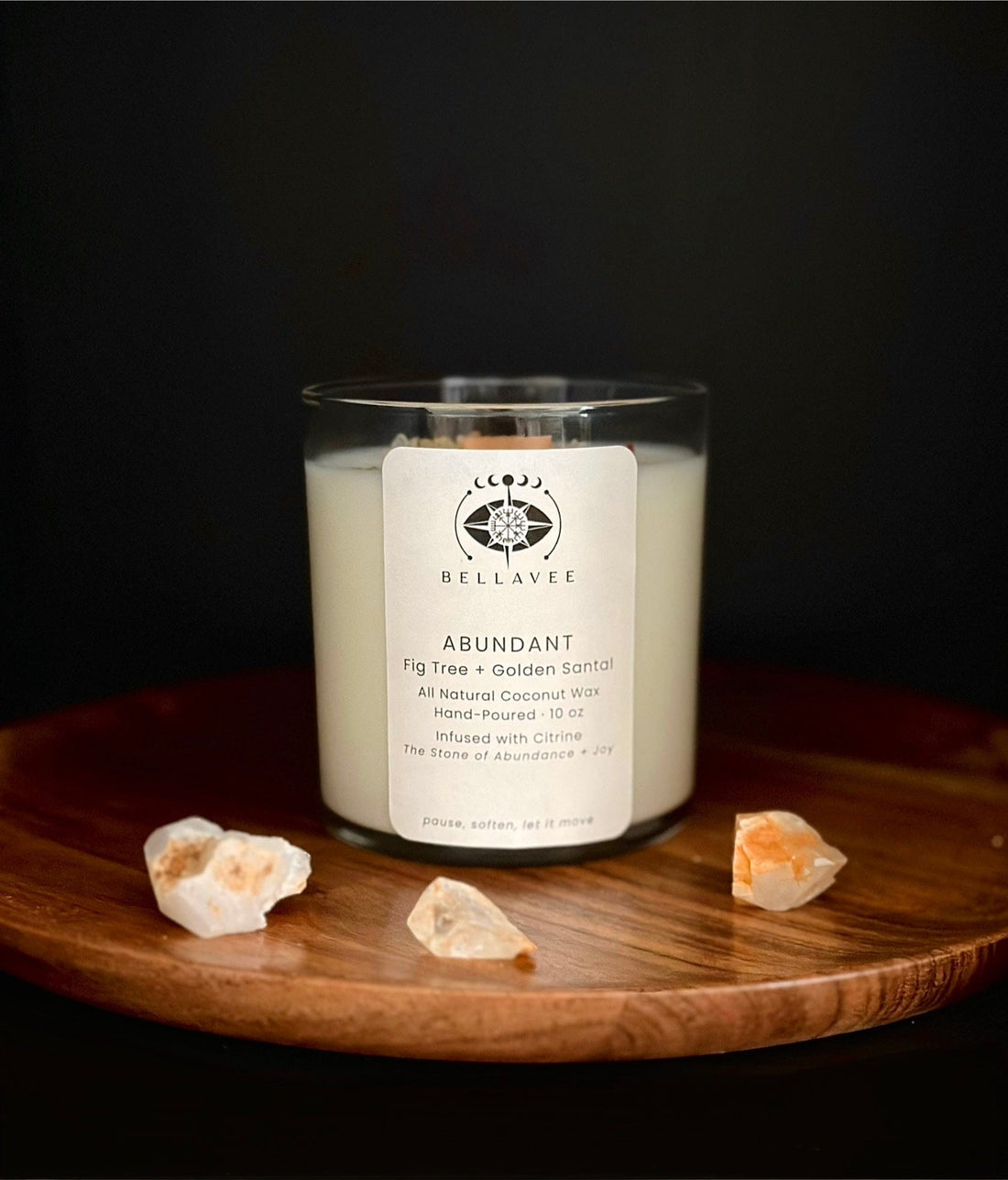Hand-poured Abundant ritual candle in a clear glass vessel infused with citrine crystals, styled on a wooden surface against a dark background.