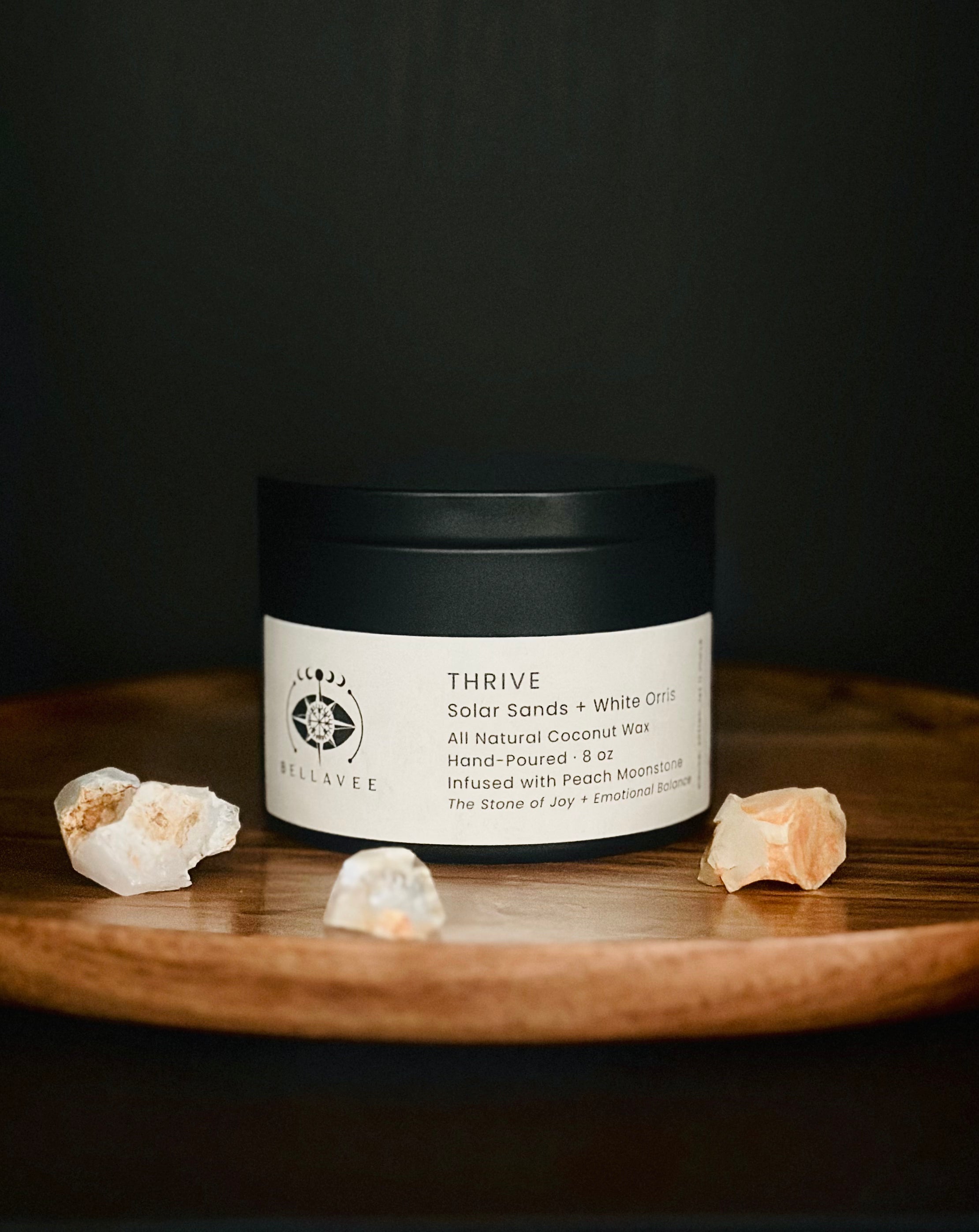 Thrive Peach Moonstone crystal ritual candle tin in a metal tin on a wooden surface.