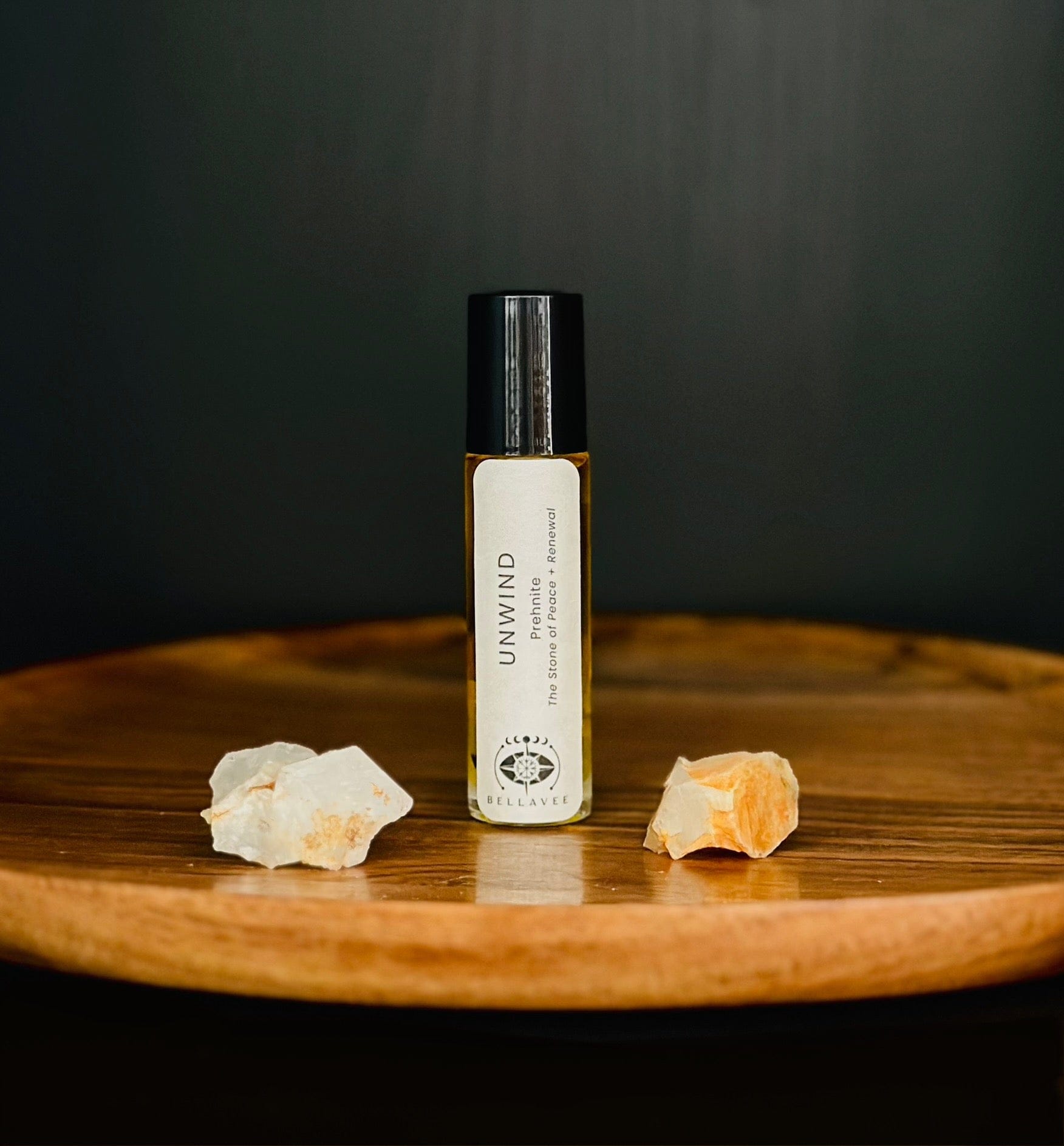 Crystal-infused essential oil roll-on labeled “Unwind” with Prehnite stones on a wooden surface.