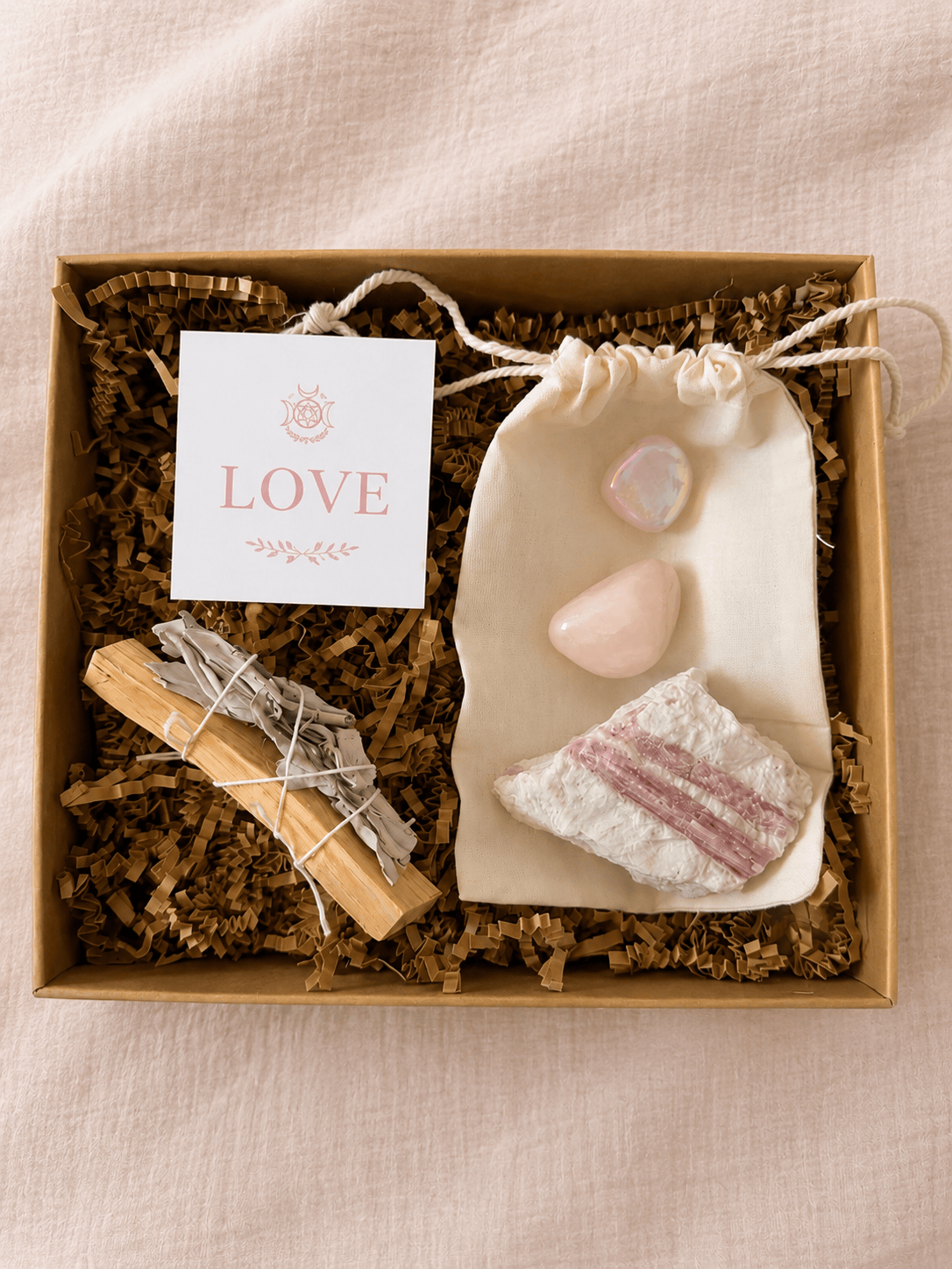 BellaVee Love Ritual Kit featuring rose quartz, raw pink tourmaline, palo santo, white sage, and a guided ritual card in a kraft gift box.