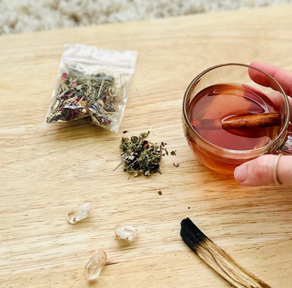 Hand holding moon tea near ritual items on a soft pink background.