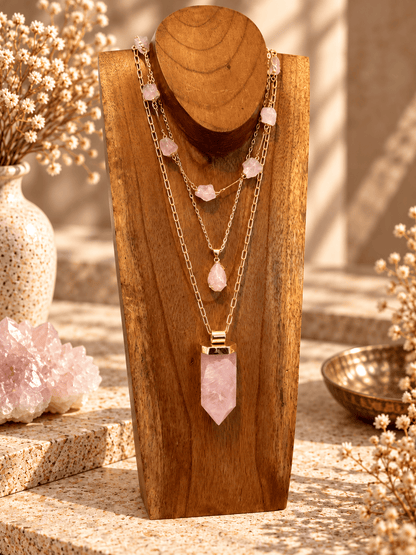 Rose Quartz teardrop pendant necklace layered with gold crystal necklaces on a wooden jewelry stand