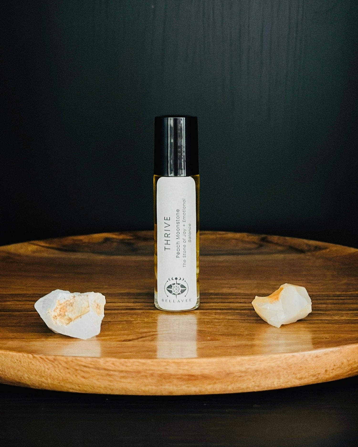 Crystal-infused essential oil roll-on labeled “Thrive” with Peach Moonstone stones on a wooden tray.