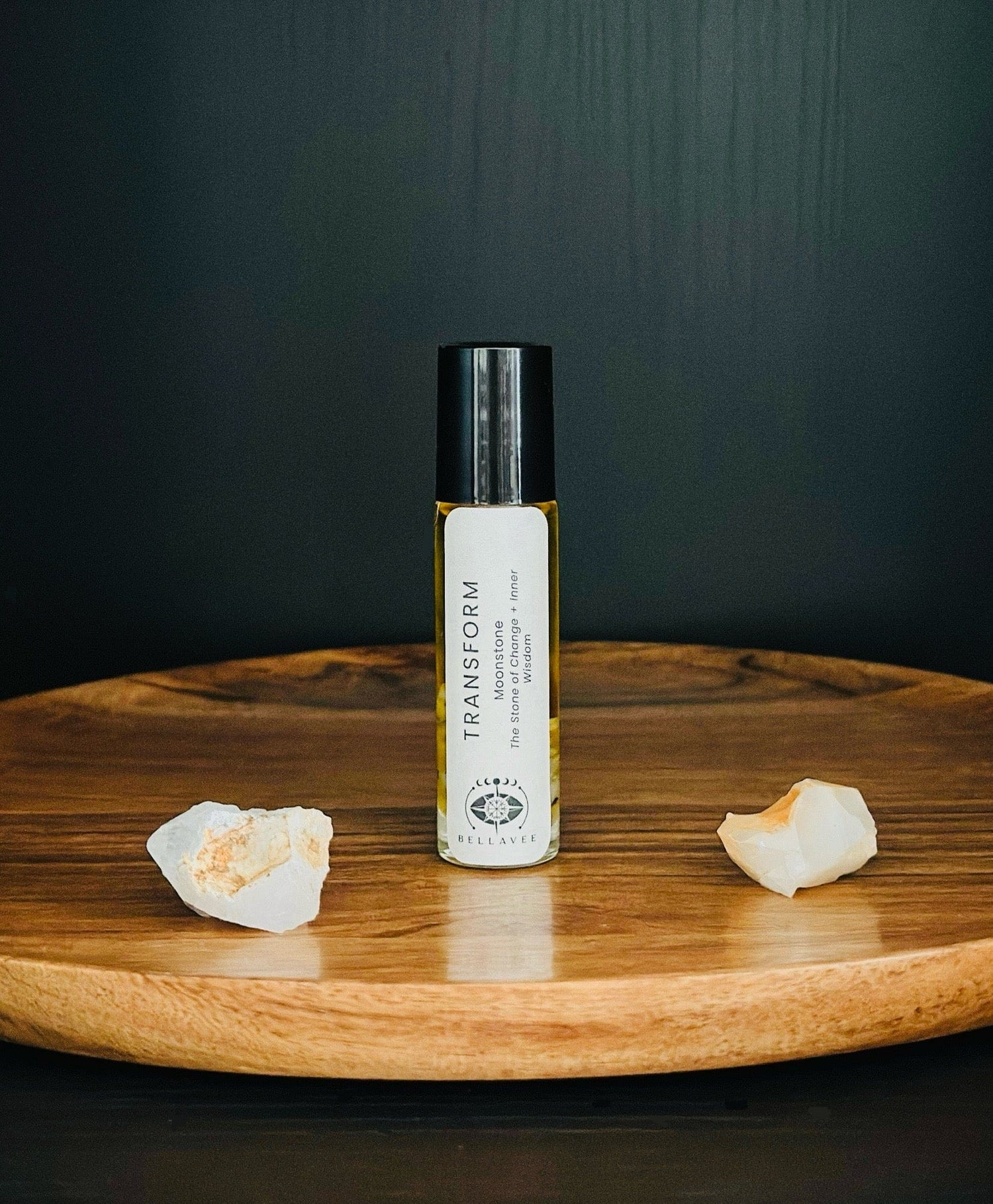 Crystal-infused essential oil roll-on labeled “Transform” with Moonstone stones on a wooden surface.