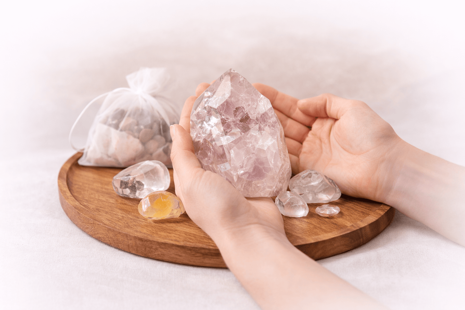 Person holding a large crystal on a wooden tray with smaller crystals and a bag of stones.