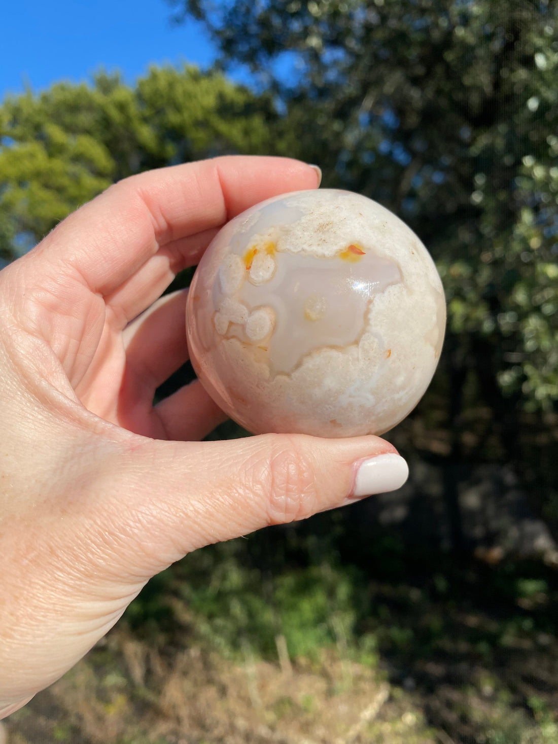Flower Agate Sphere glows beautifully under the sun, showcasing soft pink, cream, and orange floral patterns for a mesmerizing look