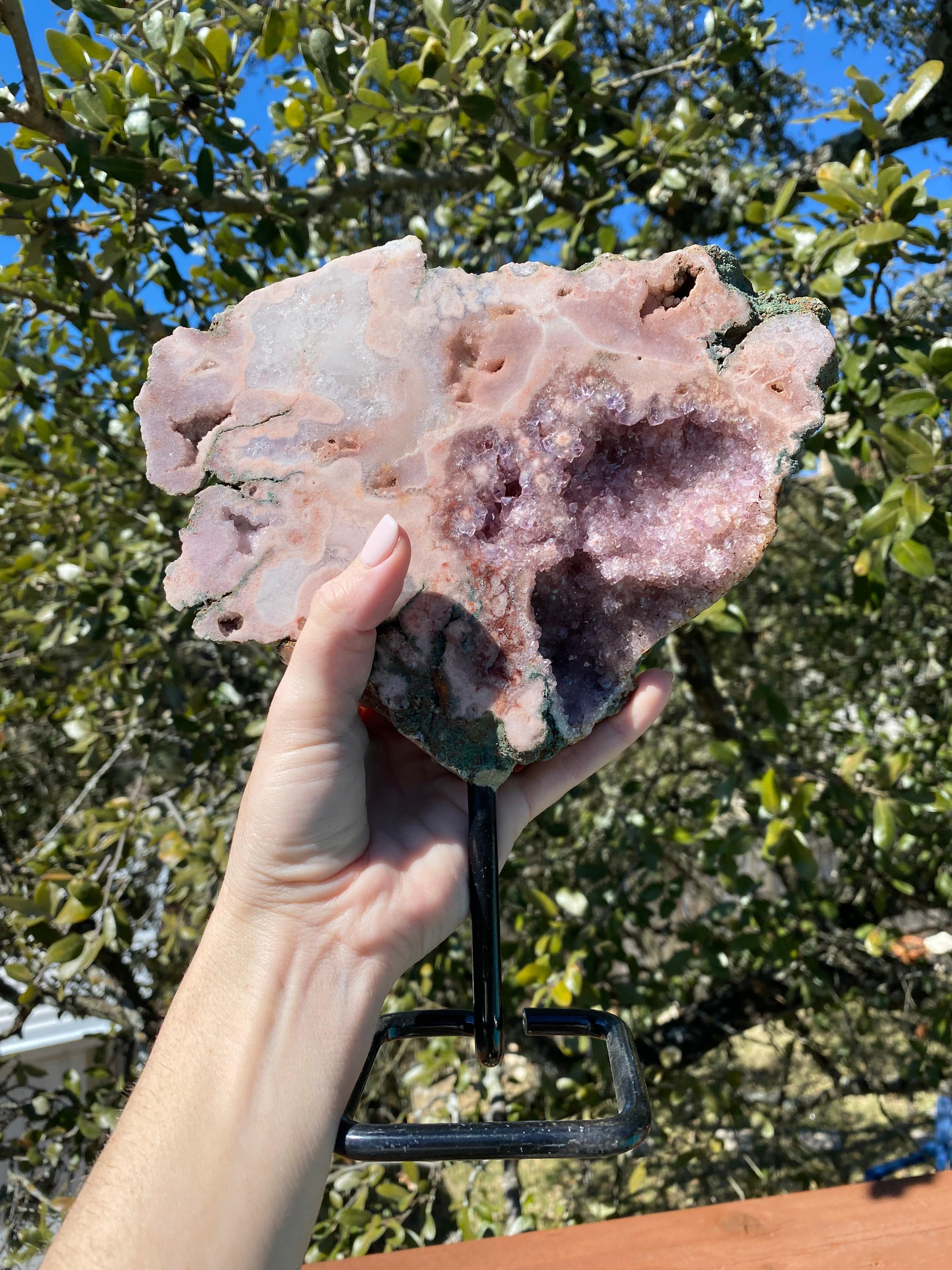 Held under sunlight, the Rose Amethyst Freeform showcases its vibrant geode cavities, filled with sparkling quartz crystals