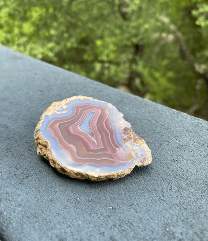 Cross-sectional Brazilian Agate slice with bands of blue, purple, gold, and rose, promoting harmony for the body, mind, and spirit.