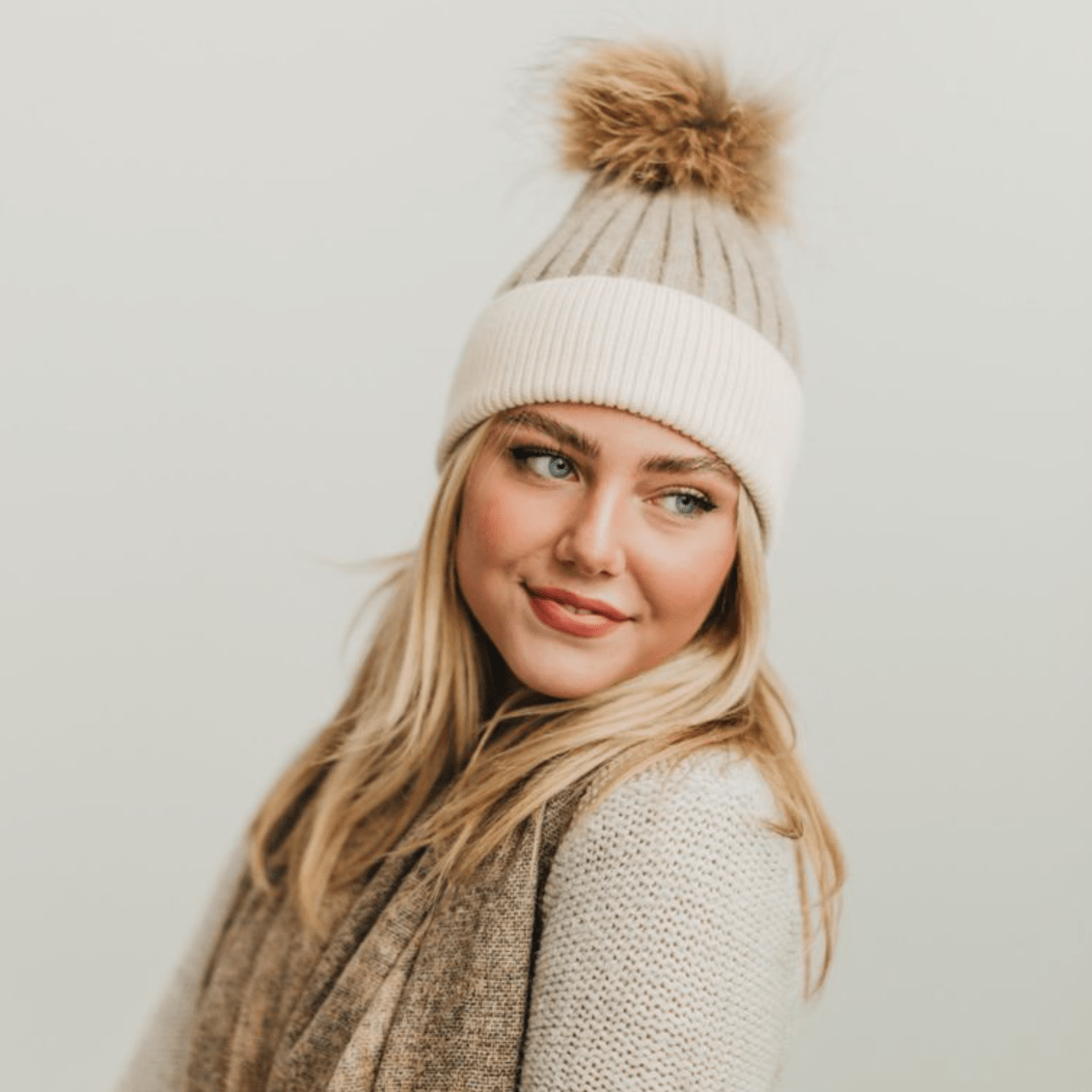 Model wearing a two-tone Angora fur pom beanie with raccoon fur pom, showcasing its softness and winter style.